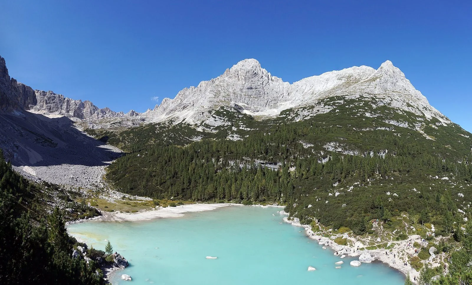Il Lago di Sorapis con l'acqua turchese ai piedi delle pareti chiare del Sorapiss e boschi di conifere