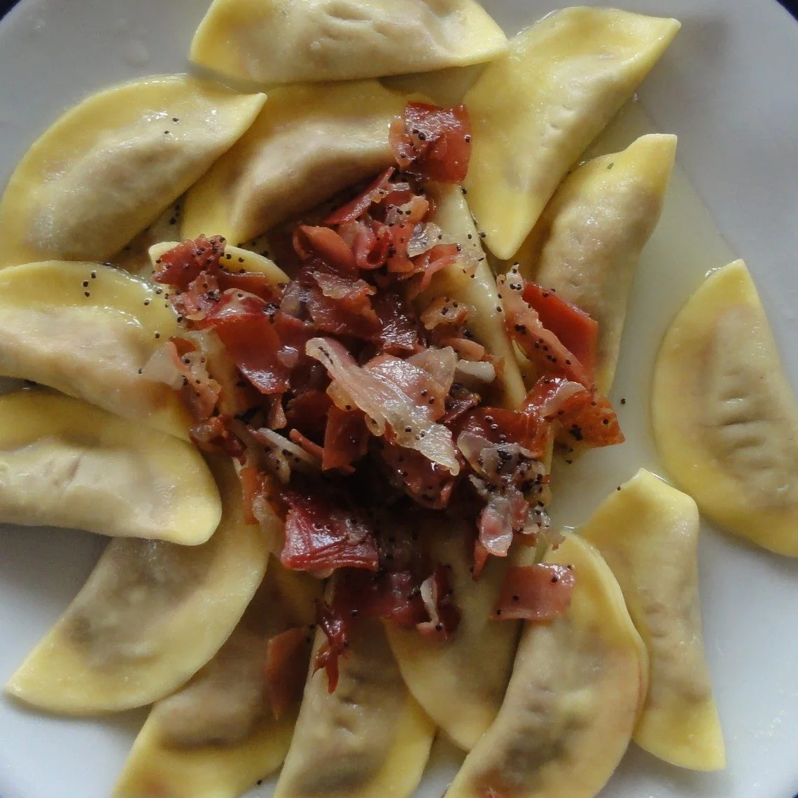Piatto di casunziei, ravioli a mezzaluna ripieni di rapa rossa, conditi con burro fuso, semi di papavero e speck croccante