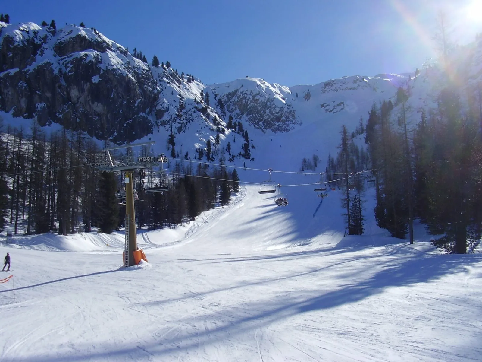 Pista da sci innevata e seggiovia tra larici e pareti rocciose sul Faloria a Cortina d'Ampezzo in una giornata di sole